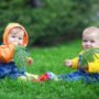 Cute twins babies sitting on fresh green grass in park