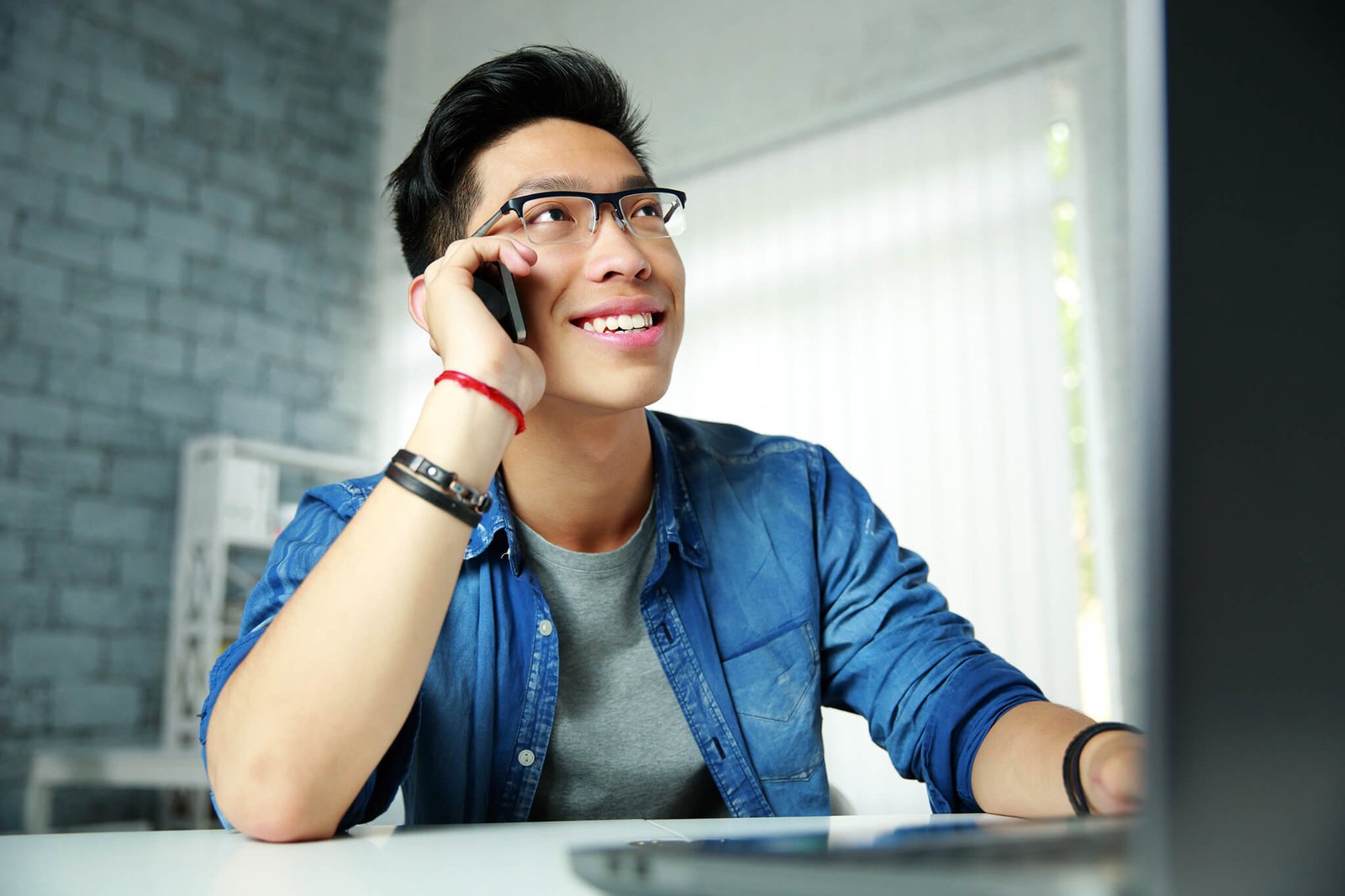 Young happy asian man talking on the phone at his workplace in office